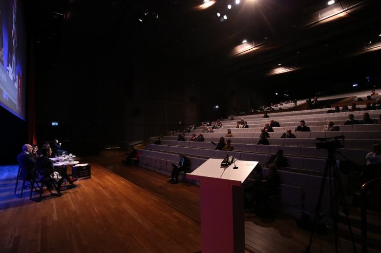 Paneliści na scenie i częściowo zapełnione audytorium, widok z boku