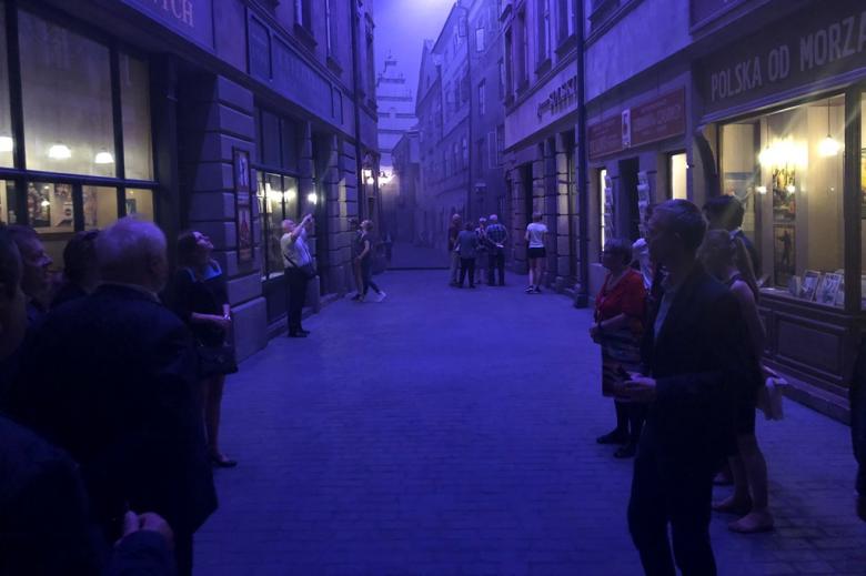 Ludzie w ciemnym pomieszczeniu, którego scenografia przypomina przedwojenną ulicę
