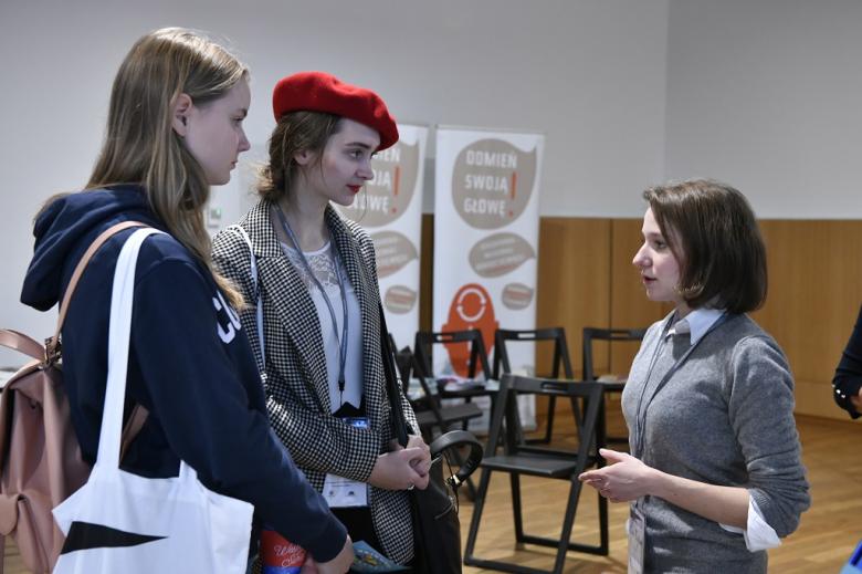 Młode kobiety rozmawiają przy rejestracji. Jedna ma wiśniowy beret