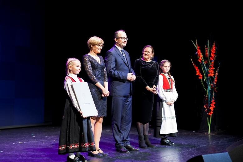 Troje dorosłych i dwie dziewczynki w norweskich strojach stoją na scenie