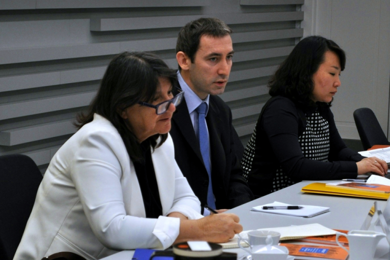 zdjęcie: dwie kobiet siedzą przy stole, pomiędzy nimi siedzi mężczyzna, kobieta na pierwszym planie jest w białym żakiecie