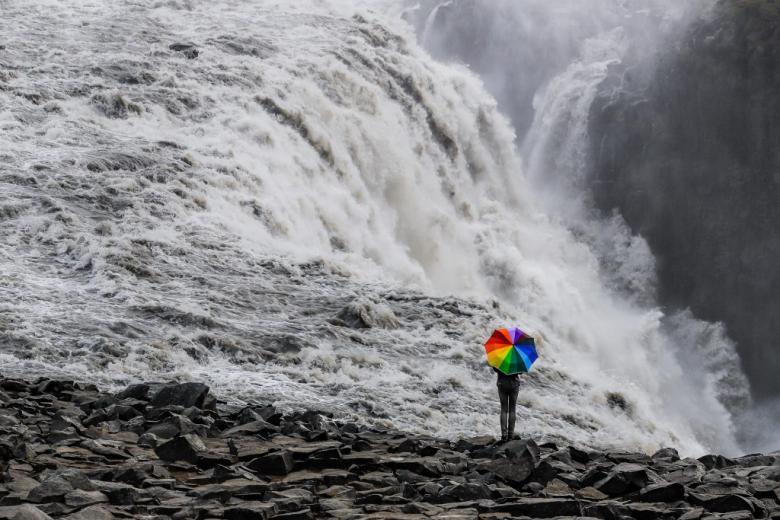 Osoba z tęczową parasolką wobec wzbierającej fali wodospadu