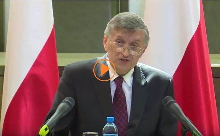 zdjęcie: mężczyzna w garniturze przemawia, za nim widać polskie flagi