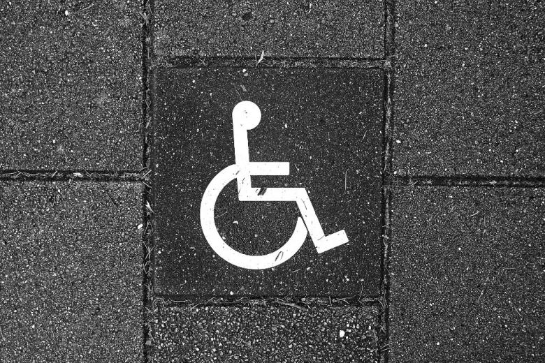 Znak pierwszeństwa dla osoby z niepełnosprawnością na szarym chodniku