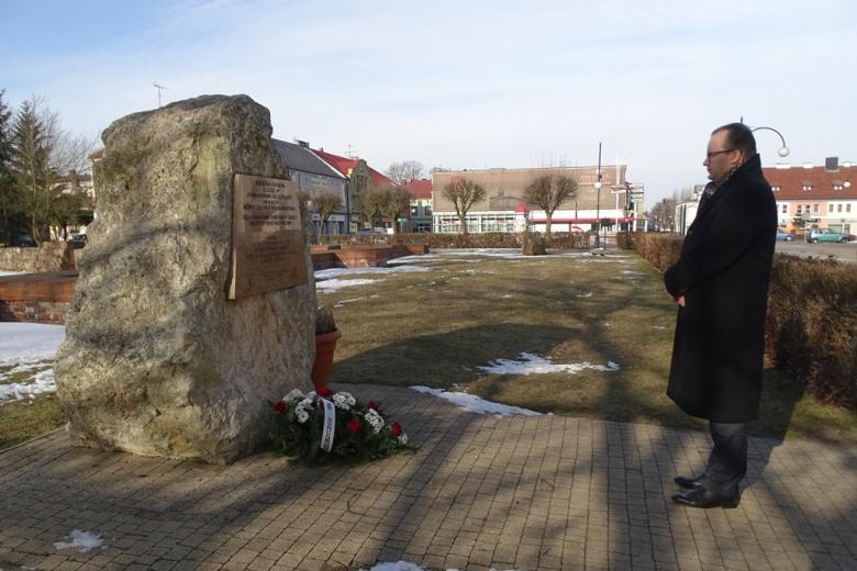 Mężczyzna stoi przed pomnikiem, przed którym leżą kwiaty, krajobraz zimowy