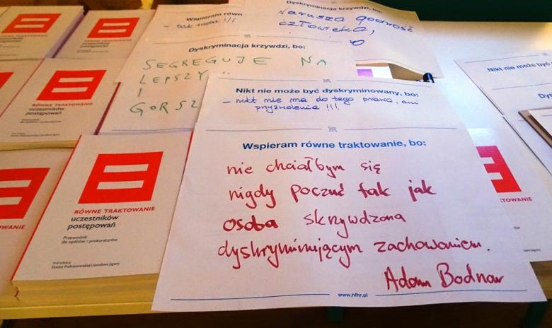 Zdjęcie stołu: kartka z drukowanym napisem "Wspieram równe traktowanie, bo ..." uzupełniona odręcznie czerwonym flamastrem: "nie chciałbym się nigdy poczuć jak osoba skrzywdzona dyskryminującym zachowaniem. Adam Bodnar"