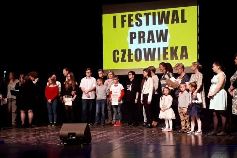 zdjęcie: na scenie stoi kilkadzisiąt młodych osób za nimi napis: I Festiwal Praw Człowieka