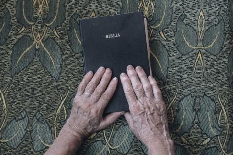 Biblia, której dotykają dłonie starszej osoby  
