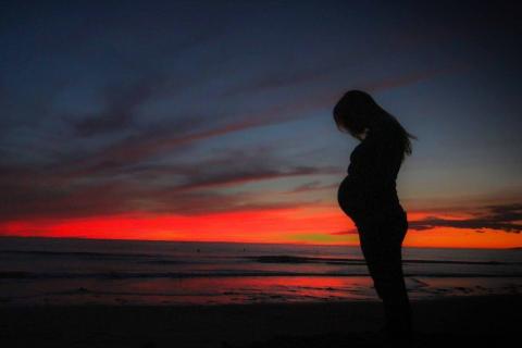 Zdjęcie kobiety w ciąży na tle zachodzącego słońca