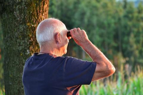 osoba starsza patrzy przez lornetkę w lesie 
