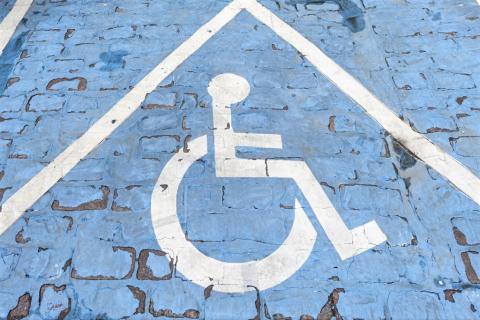 Biały znak niepełnosprawności na niebieskim tle namalowany na miejscu parkingowym