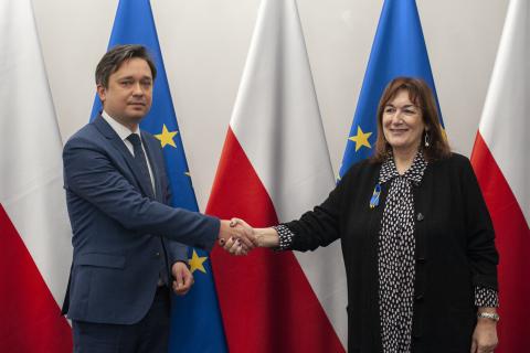 RPO Marcin Wiącek oraz wiceprzewodnicząca Komisji Europejskiej Dubravka Šuica ściskający dłonie na tle flag Polski i Unii Europejskiej