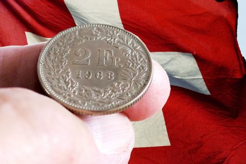 zdjęcie monety trzymanej w palcach na tle flagi szwajcarskiej 