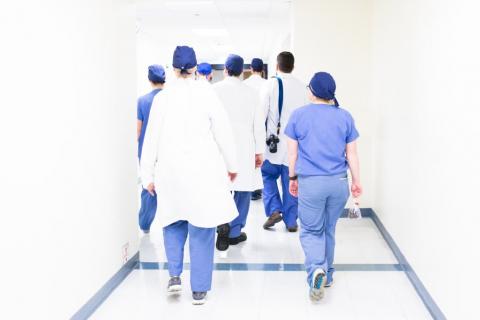 Grupa osób w kitlach lekarskich idących korytarzem szpitalnym