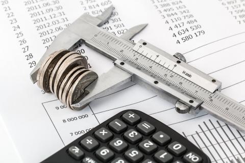 zdjęcie kalkulatora i suwmiarki z monetami na tle dokumentów finansowych