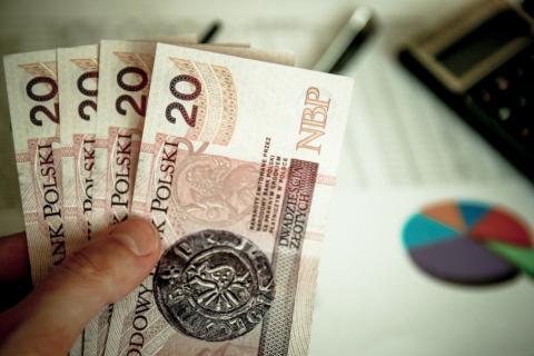 zdjęcie dłoni trzymającej plik polskich banknotów 