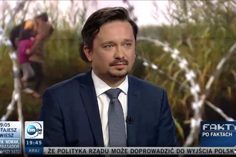 Zrzut ekranu programu telewizyjnego przedstawiający RPO Marcina Wiącka siedzącego w studiu na tle wyświetlacza prezentującego zdjęcie zasieków rozstawionych w lesie