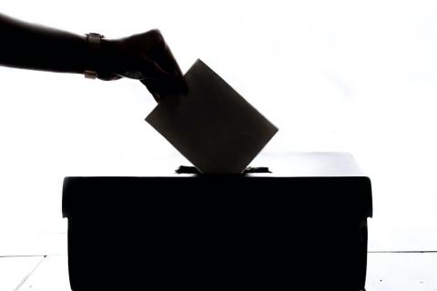 Dłoń wrzuca kartę do urny wyborczej 
