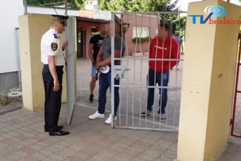 Stopklatka z nagrania - Trzech mężczyzn, jeden z megafonem, stoi za bramą, która jest zamykana przez strażnika miejskiego