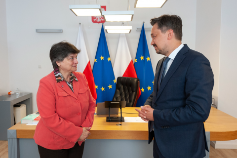 RPO Marcin Wiącek i ambasador Bułgarii rozmawiają stojąc przed biurkiem w gabinecie RPO. W tle godło Polski i flagi Polski i Unii Europejskiej