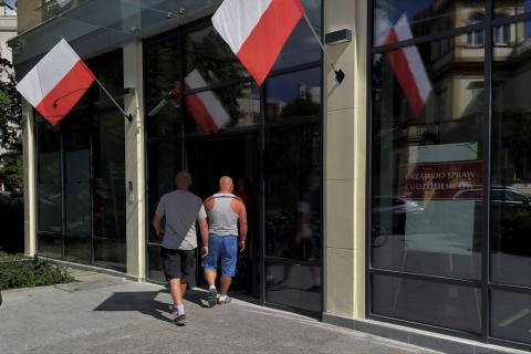 dwie osoby wchodzą do urzędu z polskimi flagami 