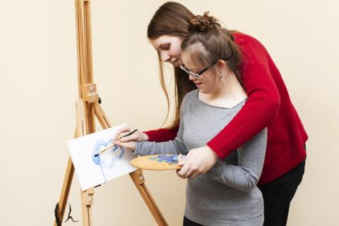 Nastolatka z trisomią 21 maluje obraz z pomocą dorosłego opiekuna