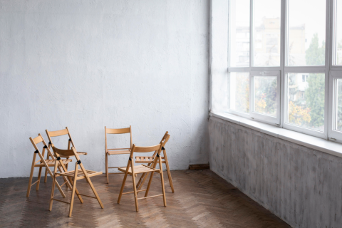 Sześć pustych krzeseł ustawionych w okrąg w pustym pomieszczeniu z jasnymi ścianami i dużym oknem