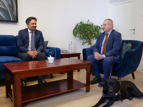 RPO Marcin Wiącek i minister Paweł Wdówik siedzą przy stoliku kawowym w gabinecie RPO i rozmawiają. U stóp ministra leży pies przewodnik.