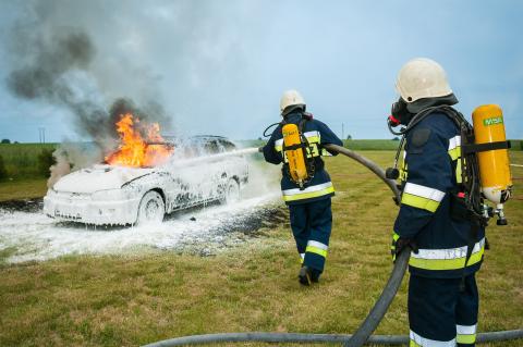 Dwóch strażaków gasi płonący samochód