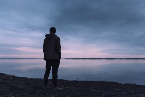 osoba stojąca na brzegu jeziora o wschodzie słońca
