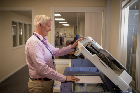 seniorka stoi przy maszynie kopiującej dokumenty