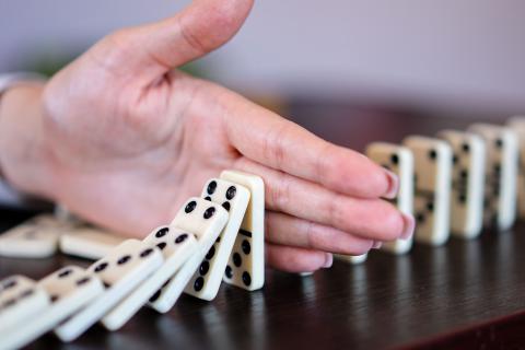 Dłoń przerywająca ciąg upadających klocków domino