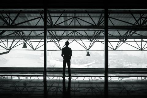 Sylwetka osoby stojącej na tle dużego okna, za którym widoczne są samoloty
