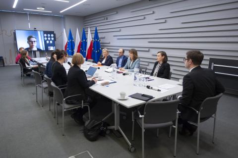 ZRPO Valeri Vachev i członkinie Inicjatywy rozmawiają siedząc przy konferencyjnym stole. W szczycie stołu stoi ekran wyświetlający uczestników spotkania łączących się za pośrednictwem internetu. Obok ekranu stoją flagi Polski i Unii Europejskiej