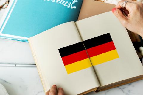 Dłonie trzymające na stole otwartą książkę, w której jest narysowana duża flaga niemiecka