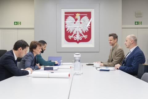 Pięć osób siedzi po dwóch stronach stołu konferencyjnego, w tle godło Polski