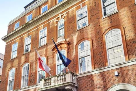 Wielopiętrowa, ceglana kamienica z widocznymi flagami Polski i Unii Europejskiej zawieszonymi na balkonie