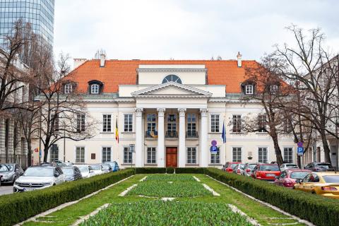 Elewacja klasycystycznego dwupiętrowego pałacu z czterema kolumnami wspierającymi portyk nad wejściem, przed wejściem na masztach flaga Belgii i flaga UE
