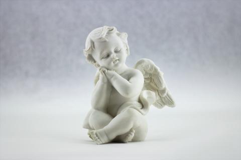 Jasna, kamienna figurka małego aniołka siedzącego po turecku