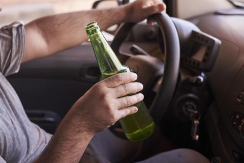 Butelka piwa w rękach mężczyzny prowadzącego samochód w ciągu dnia