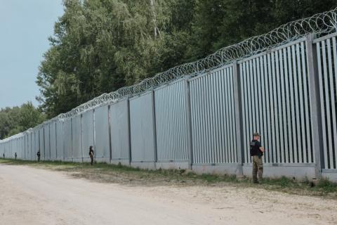 wysoki płot na granicy przy którym w pewnej odległości od siebie stoją strażnicy