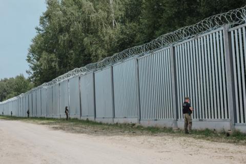 wysoki płot na granicy przy którym w pewnej odległości od siebie stoją strażnicy 