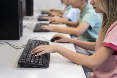 Uczniowie szkoły siedzący w ławce i korzystający z komputerów podczas zajęć