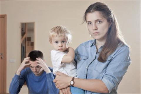 Smutna kobieta trzymająca dziecko na rękach i smutny mężczyzna trzymający się za głowę