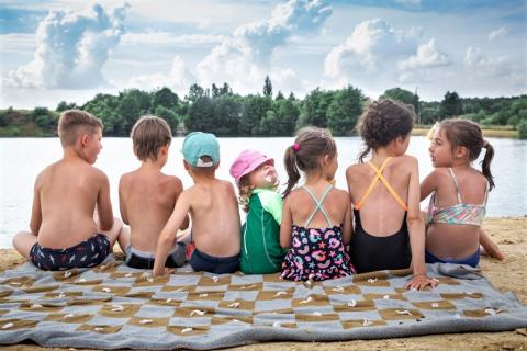 siedmioro dzieci siedzi nad jeziorem odwrócone tyłem