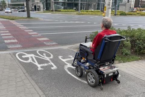 Osoba na wózku elektrycznym czeka przed przejściem dla pieszych 