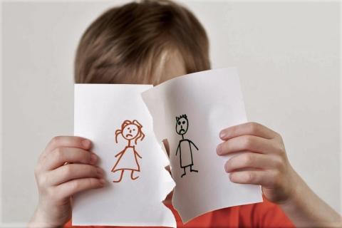 dziecko z twarzą zasłonięta rozdartym rysunkiem mamy i taty