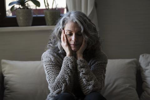 Smutna starsza kobieta siedzi na kanapie i trzyma głowę w dłoniach