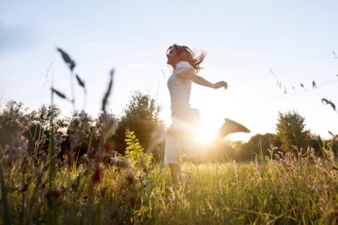 kobieta biegnie przez łąkę na tle słońca 