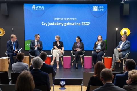 Sześć osób siedzi na krzesłach na scenie, w tle na wyświetlaczu biały napis na niebieskim tle "Czy jesteśmy gotowi na ESG"